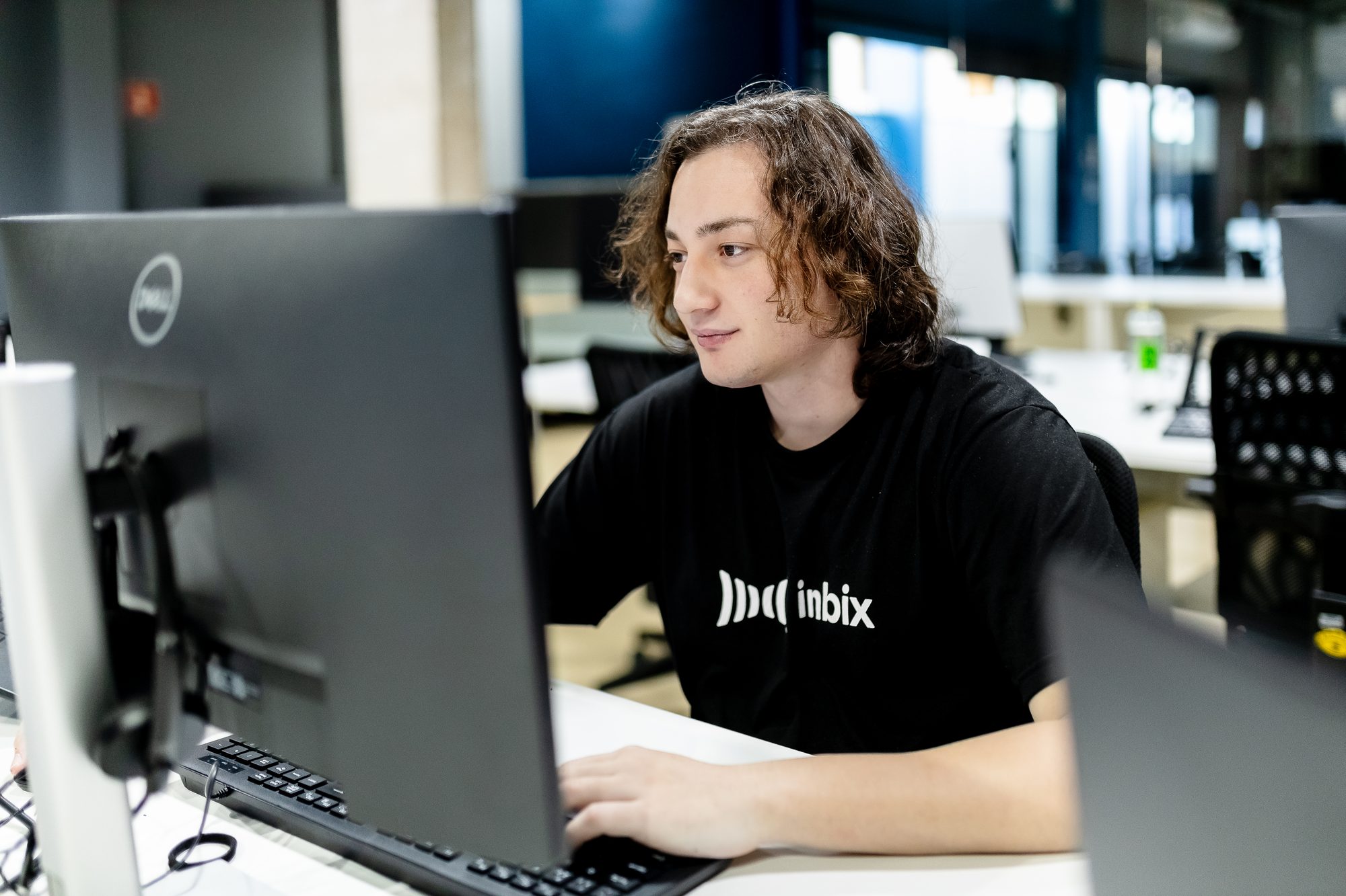 Profissional de camiseta da Inbix trabalhando ao computador no escritório