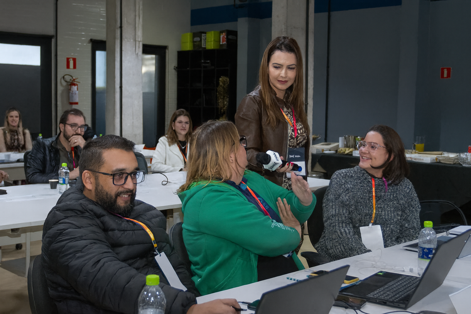 Facilitadora com microfone conduzindo dinâmica entre os participantes sentados