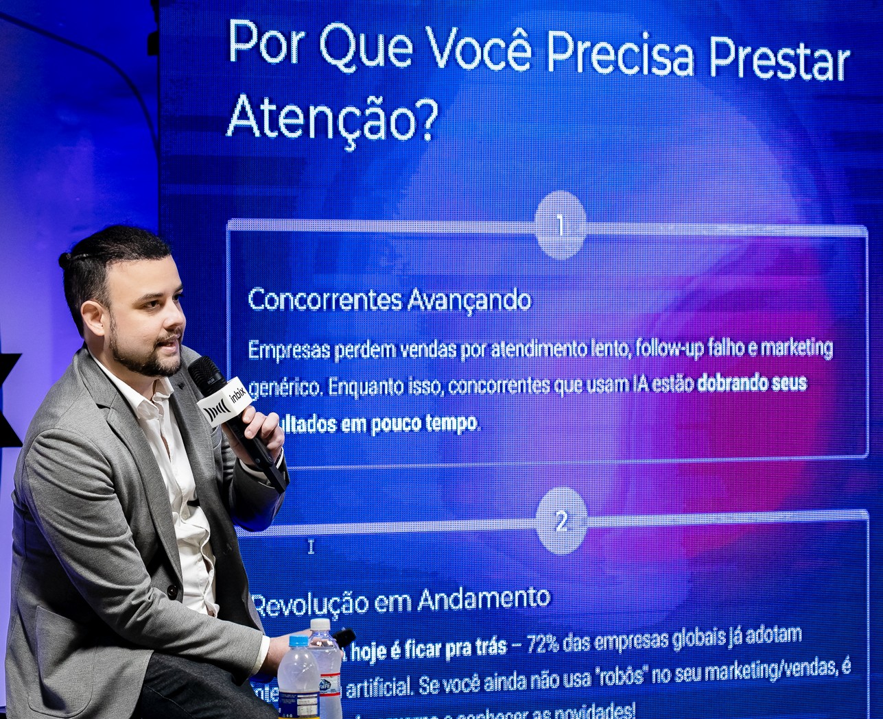 Palestrante ao lado do slide Por que você precisa prestar atenção, sobre concorrência e IA