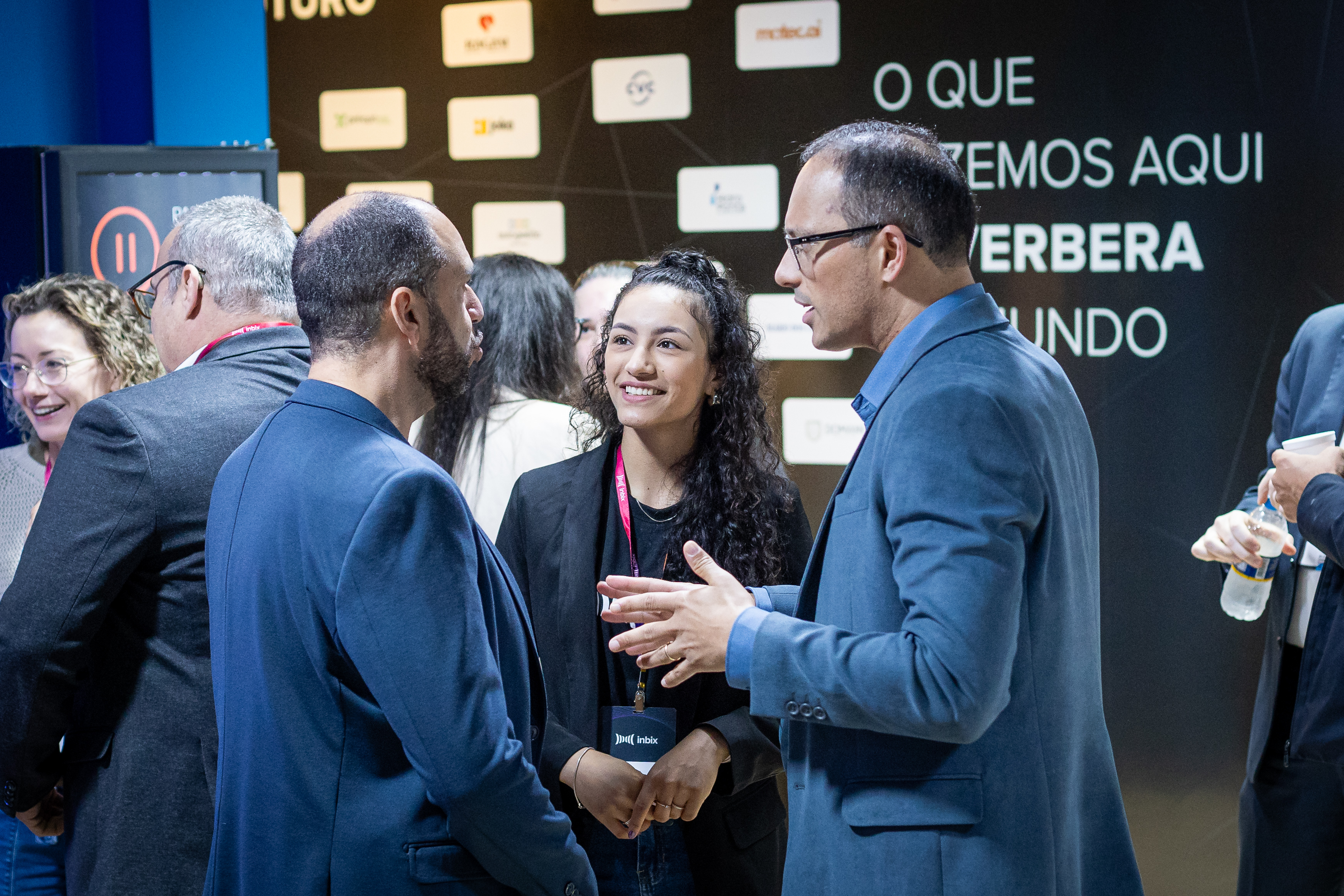 Profissionais conversando em evento diante do painel O que fazemos aqui reverbera no mundo